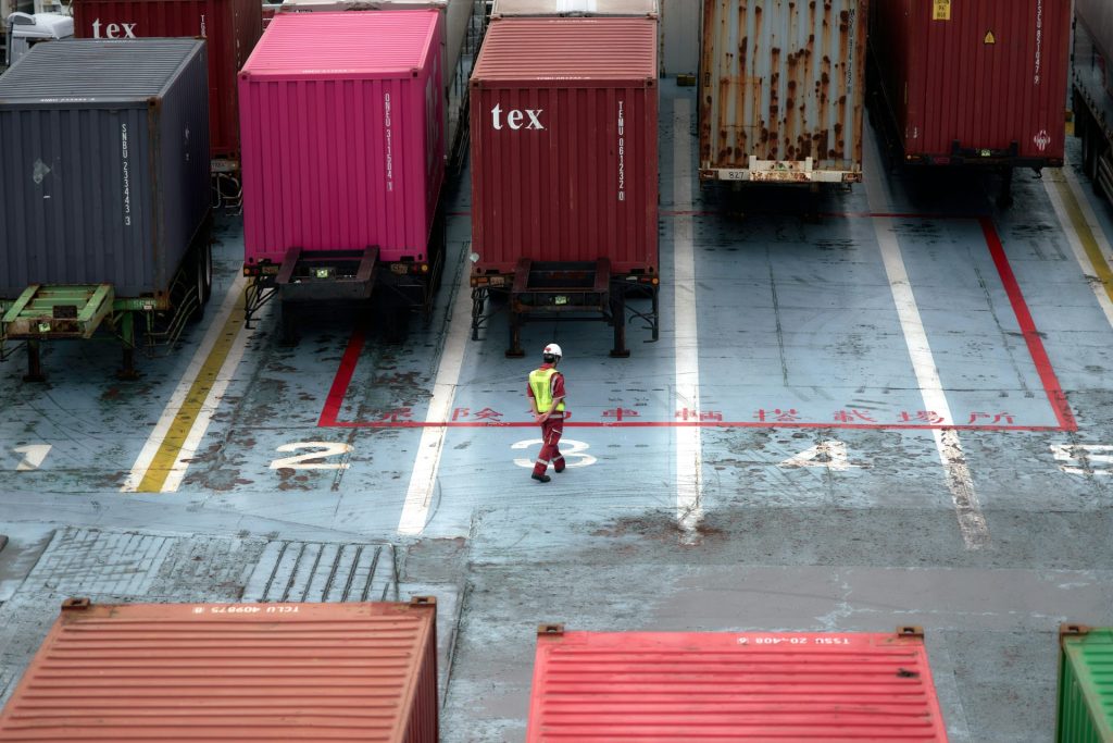 Un homme se tient debout sur un parking à côté de nombreux conteneurs maritimes.